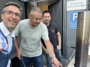 Drei Männer stehen im Freien vor einem Pizza-Ofen.